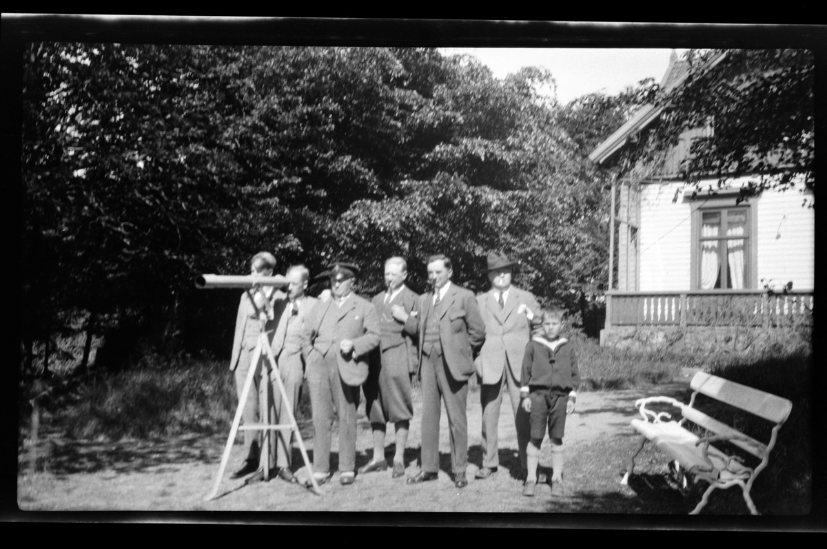 Seks menn og en gutt ved en kikkert plassert i hagen til familien Sundts sommerhuset på Farøy, Farsund. Fra venstre Bjarne, Peter, Halfdan og Finn Sundt, Johan Buratti, Trygve Sundt og Bjørn Reymert. Fotografert mai 1928.