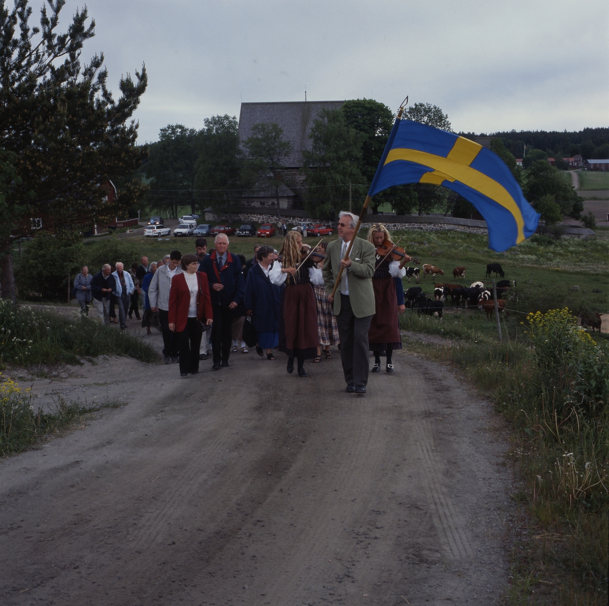 Kyrkvandring i Trönö, söndagen 17 juni 2001. Främst i ledet går en man med fana och efter honom går "Spelsystrarna" med sina fioler. Därefter går resten av deltagarna.