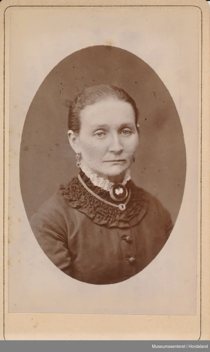 portrettfotografi av kvinne med oppsatt hår, mørk kjole med rysjekrage, blonde og medaljong i halsen