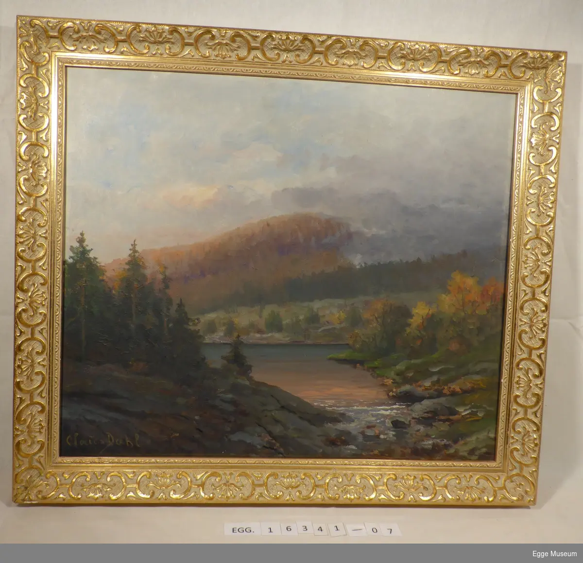 Maleriet viser et elveutløp fra en innsjø, med skogkledte fjell, skyer og trær med høstfarger i bakgrunnen. Til venstre i bildet er det grantrær som vokser på berget inntil elveutløpet.