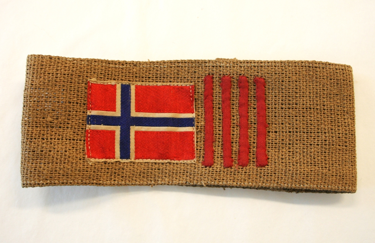 Armbindet har det norske flagget etterfulgt av fire vertikale røde striper.