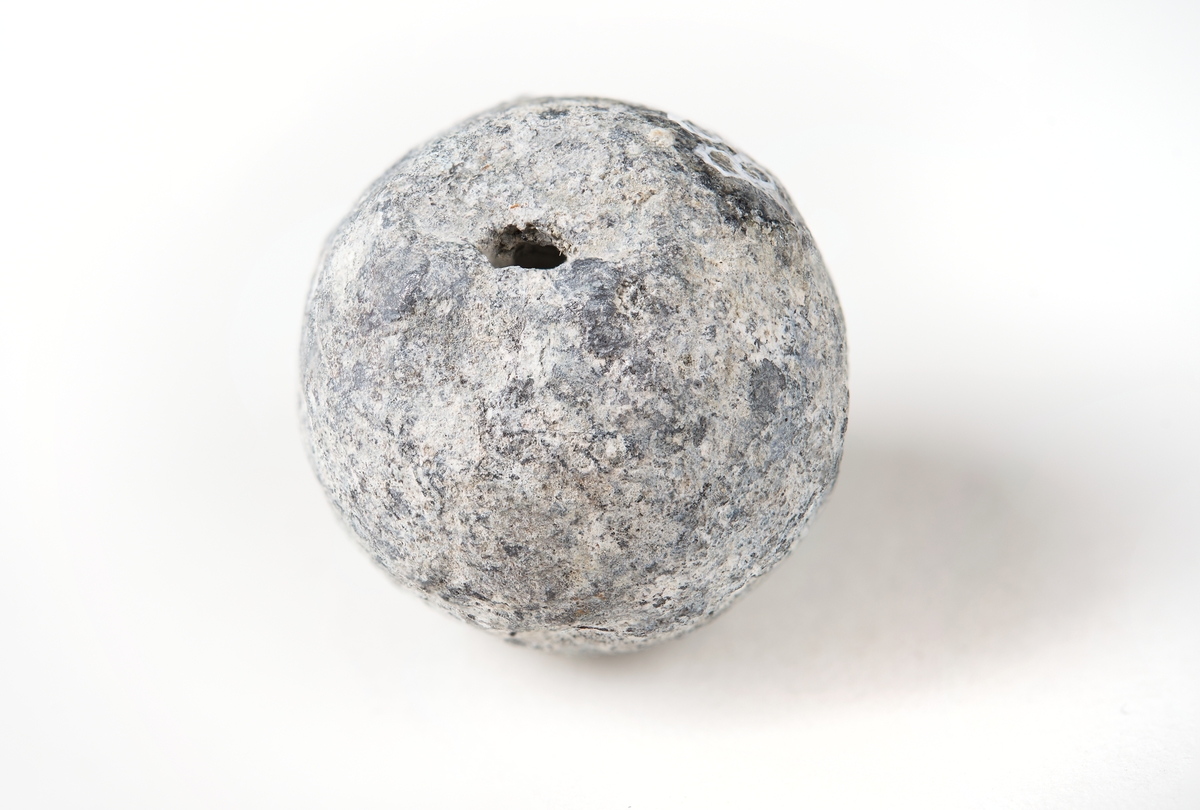 Muskötkula av bly med gjutskarv och en inborrning. Hålet har en diameter på 1,8 mm och är 8 mm djupt.