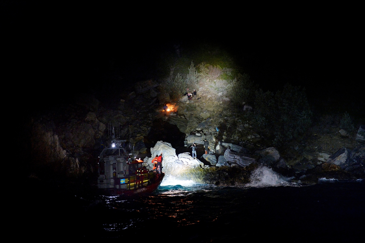 Svenska sjöräddningssällskapets båt lyser upp en klippavsats med människor.