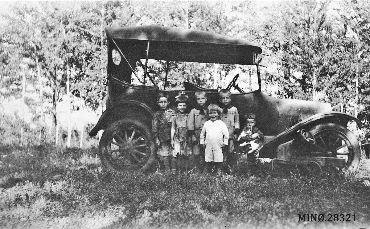 Seks smårollinger og en pusekatt foran gammel bilmodell
"Hornseth & Jacklin family at the Homestead"