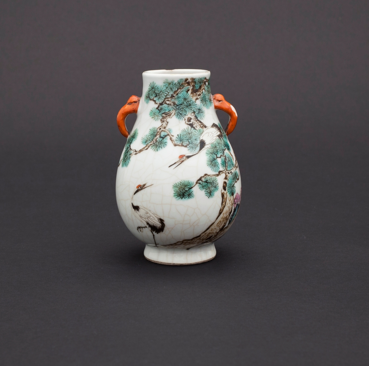 Famille rose vase med kirsebærblomst, furutrær, stein og traner. Tranen fremstilles ofte i kombinasjon med furu og stein, og er som oftest brukt som et symbol for langt liv. Håndtakene er utformet som elefanthoder.