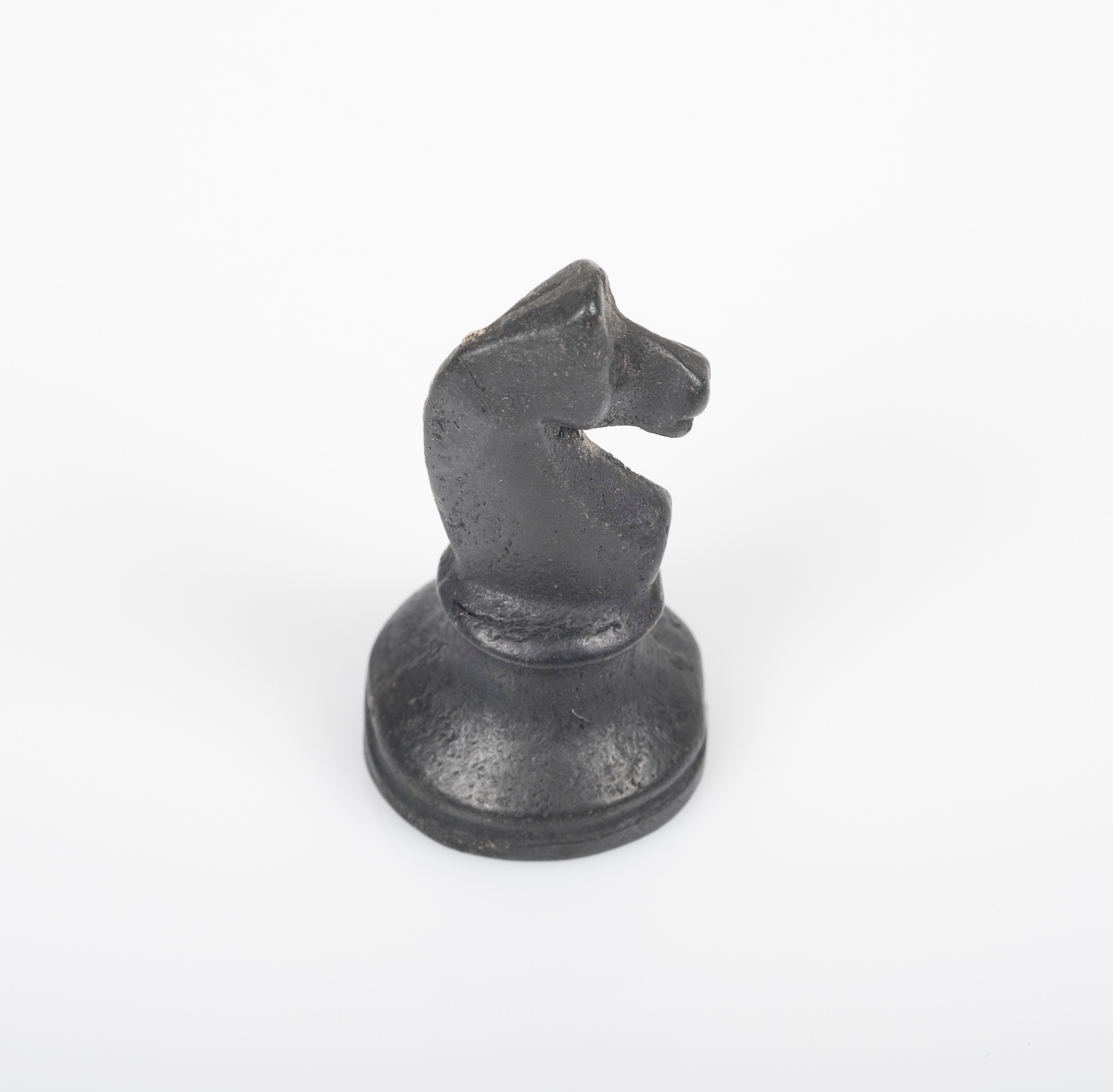 Sjakkbrikken (springer) er laget av tre, og er malt svart. Et lite avlangt hull på undersiden.