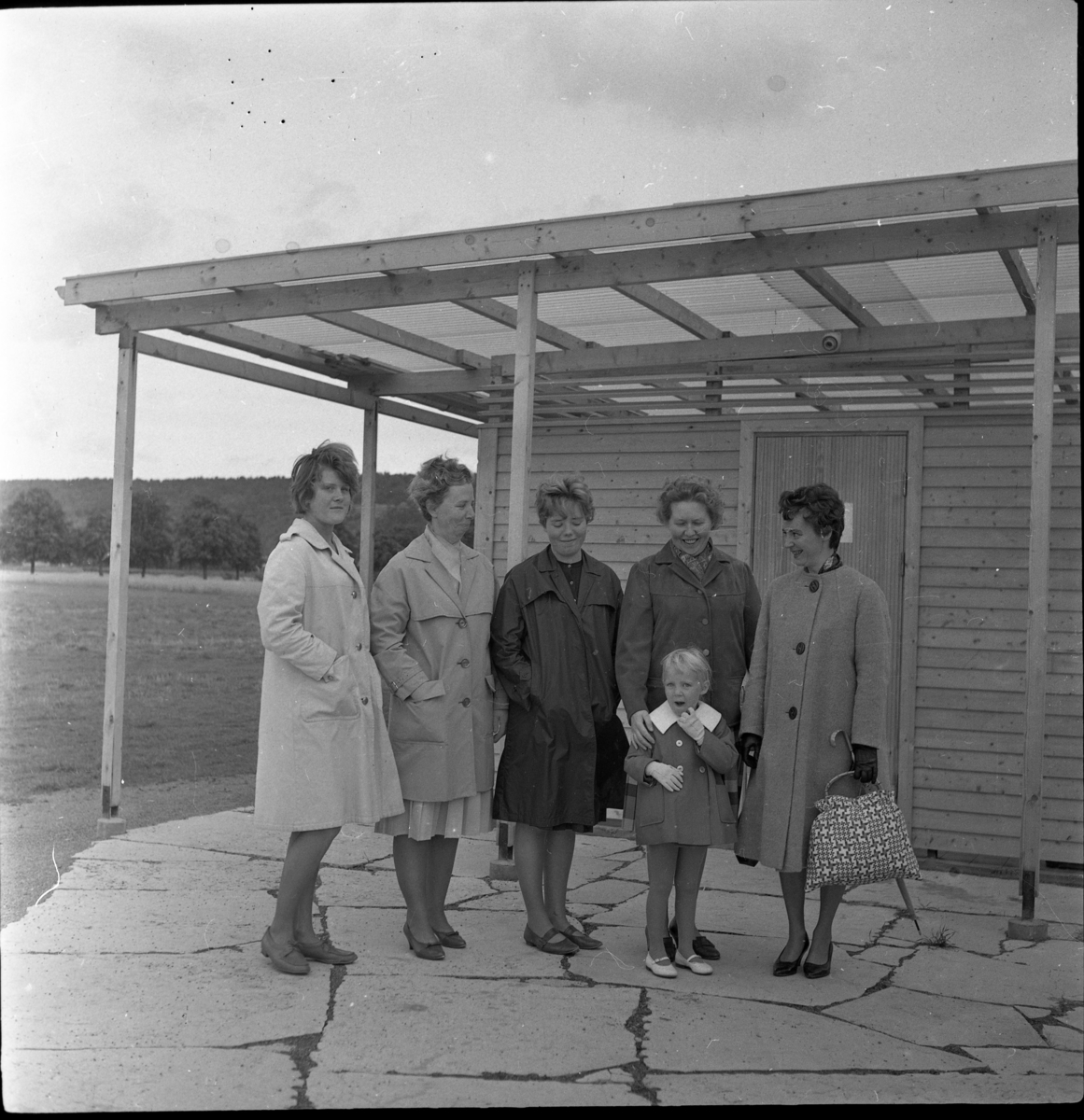 Fem kvinnor och en liten flicka stående framför en byggnad med strykrum vid Gränna camping. Fr vänster: Eva Heldebrandt, Alice Johansson och hennes dotter Birgitta Johansson samt Britta Blixt som har sin ena hand på en liten flickas axel. Kvinnan till höger är inte identifierad
