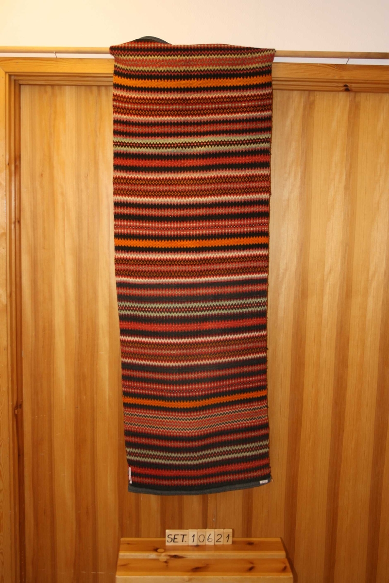 Rektangulært teppe med mønster, falda  og påsydd kanting i båe endar.