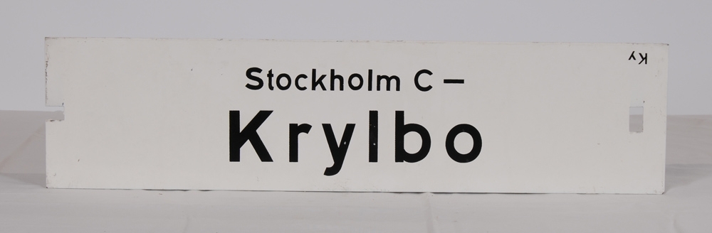 Destinationsskylt av plåt med vitmålad botten och svart schablonmålad text. På ena sidan står det: Stockholm C-Krylbo, på andra sidan: Krylbo-Stockholm C. Slutdestinationen har större text. På den sida som det står "Stockholm C-Krylbo" står det även "Ky" uppochnedvänt i överkanten. I ena ändan av skylten finns ett rektangulärt jack och i andra änden ett rektangulärt hål.