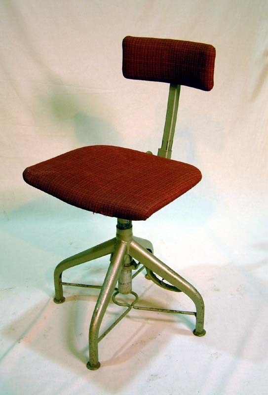 Så kallad skrivbordsstol eller snurrstol. Stoppad sits klädd med ylletextil, röd med tunna svarta ränder som mönster. Sitsen sitter på ett stålrör som i sin tur sitter i ett underrede av stål med fyra stolsben. Sitsens undersida av trä. Ryggstöd bestånde av fyrkantigt stålrör med rektangulär ryggtavla stoppad och klädd med samma tyg som sitsen, som går att vicka fram och tillbaka för skön ställning för ryggen. Ryggstödet även höj- och sänkbart. Längst ned på varje ben runda brickor som fungerar som stolens fötter. Tvärslåar mellan stolsbenen av hopsvetsade tunna stålrör för ökad stabilitet. På sitsens undersida är stämplat: "Kommersiella byrån".