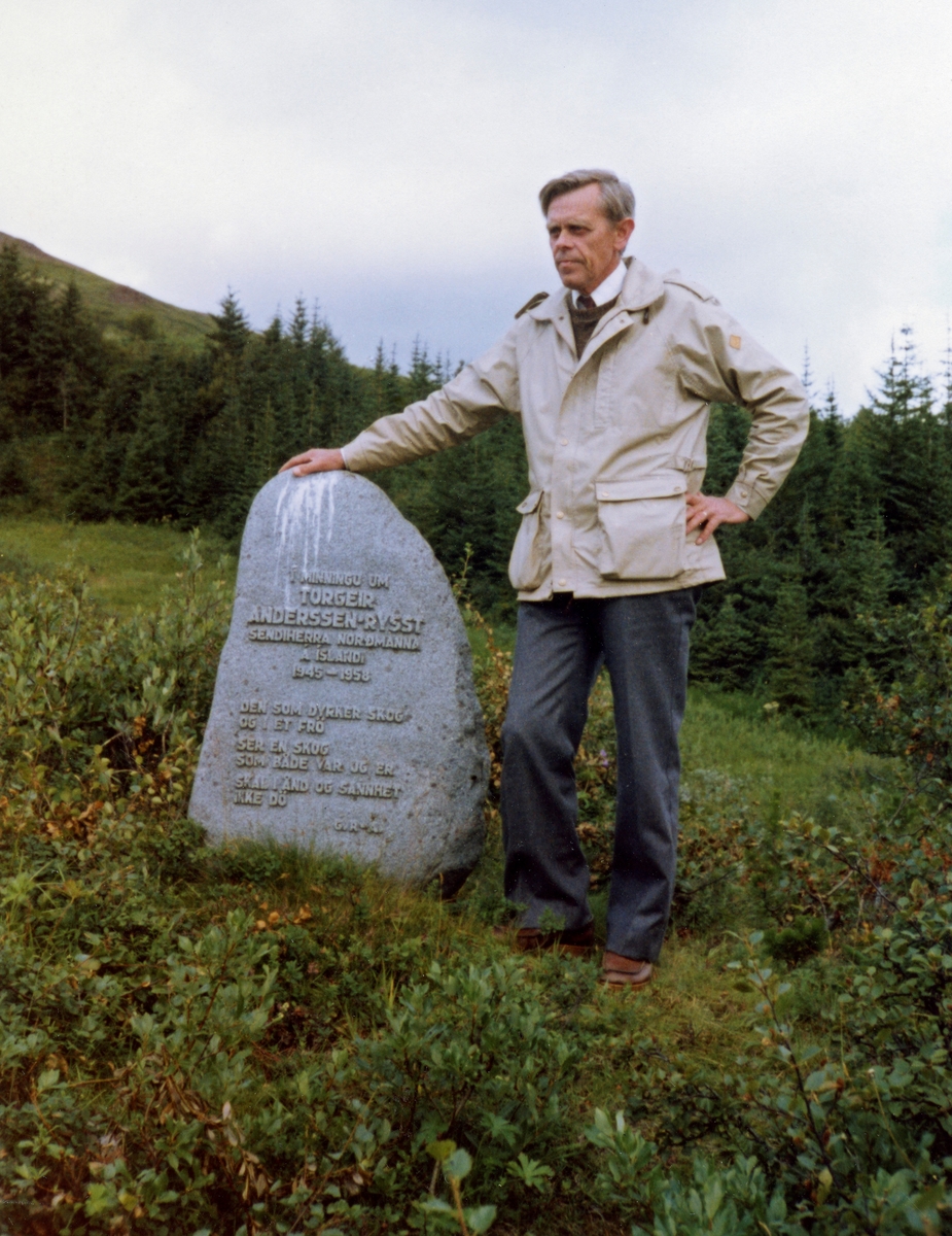 Den islandske skogfunksjonæren Garðar Jónsson (1919-2003), fotografert ved minnesmerket over ambassadør Torgeir Anderssen-Rysst (1888-1958) i Haukadalur, litt nord for Laugarvatn på Sørvest-Island i 1982.  Garðar Jónsson arbeidet i den islandske skogetaten fra 1944 til han nådde pensjonsalderen i 1986.  Han hadde gått skogskole på Island, men også hatt praksisperioder i Danmark og Norge (Alstahaug planteskole).  Da dette bildet ble tatt var han skógarvörður for Skógrækt ríkisins på Sør-Island (Suðurlandi).  Torgeir Anderssen-Rysst, som hedres på dette stedet, var sentral som tiltrettelegger i det skogfaglige samarbeidet mellom Norge og Island (se nedenfor).  Minnesmerket er en stein, reist på høykant på ei åpen flate, omgitt av plantet barskog.  Støtta ble reist i 1961.  Den har følgende tekst:  

«I minningi um 
Torgeir Anderssen-Rysst
Senherra Normanna a Island
1945-1958

Den som dyrker skog 
og i et frø 
ser en skog
som både var og er
skal i ånd og sannhet
ikke dø.» 

Torgeir Anderssen-Rysst var fra Ålesund.  Han var utdannet jurist og offiser, og arbeidet blant annet som redaktør i avisa Sunnmørsposten.  I 1925 ble Anderssen-Rysst valgt inn på Stortinget for partiet Venstre.  Som politiker var han forsvarsminister i Johan Ludwig Mowinckels regjering i perioden 1928-1931.  Etter 2. verdenskrig ble Anderssen-Rysst norsk sendemann eller ambassadør på Island, et embete han hadde fra 1945 til sin død i 1958.  Som ambassadør var Anderssen-Rysst opptatt av å legge til rette for mer samarbeid mellom Norge og Island.  Et av de viktigste samarbeidsfeltene ble skogreisinga.  Om den skrev han følgende:

«Efter mange arbeidsår på Island er min oppfatning sterkere enn noen gang tidligere blitt denne: Islendingene og de som forstår Islands behov og vil være med å dekke dem, må for all del prøve å få opp skog i landet.  Sandblåsten gjennom hundreder av år er som en kreftskade for landet.  Skog utover landet vil kunne bidra til å hindre denne.  Landets behov for trevirke er også særdeles påtrengende.  Å reise skog på Island er en så vanskelig og mektig oppgave at mange nekter å tro at det er mulig å løse den.  Men de er færre enn før.  Skogreisingsmennenes flokk er i svær vekst.  Den moderne vitenskap kommer også mer og mer til deres hjelp som er positivt innstillet på å styrke Islands eksistensmulighet gjennom skogreising.  Islendingene trenger imidlertid venner, trenger allierte til å løse denne kjempeoppgave å få skog til å vokse i Island for å verne folks nasjonale liv og sikre dets fremtid.  Ingen har i så henseende noen større oppfordring enn nordmenn.  Det var fribårne nordmenn som bygget Island i sin tid.  Her tales ennu det gamle norske mål.  Intet folk står oss nærmere – fra alle tider sett.  Her ble vår norske historie skrevet ned og vernet mot glemsel, slik at vi nordmenn kunne finne tilbake til oss selv, og derved reise oss som fritt folk igjen.

Intet folk har noensinne gjort oss nordmenn større tjenester enn islendingene.  Intet folk skylder vi mere.  Vi kan betale en del av gjelden ved nidkjært å gå inn for skogreising i Island.  Noen større tjeneste kan vi ikke gjøre dem.» (sitat fra Tidsskrift for skogbruk nr. 11 1956, side 68-69) 

Med utgangspunkt i disse oppfatningene om skogreisingas betydning organiserte Torgeir Rysst-Anderssen – samarbeid med Det norske Skogselskap og Skógræktarfélags Íslands – store utvekslingsprosjekter, der norske ungdommer reiste til Island og islandske ungdommer til Norge for å delta i skogreisinga og lære et nordisk naboland å kjenne.
