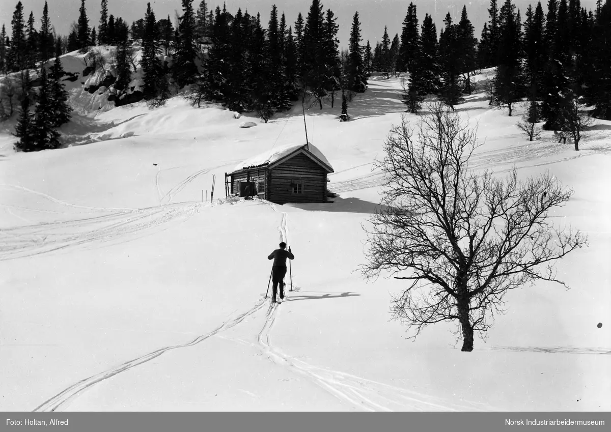 Mann på ski ved hytte.