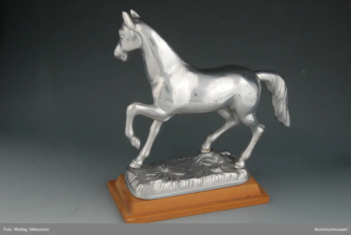 Hesteskulptur plassert på en fot. Foten har en plakett med inskripsjon
Hesten står i en aktiv posisjon med venstre forben høyt hevet, hodet løftet og vendt mot høyre.