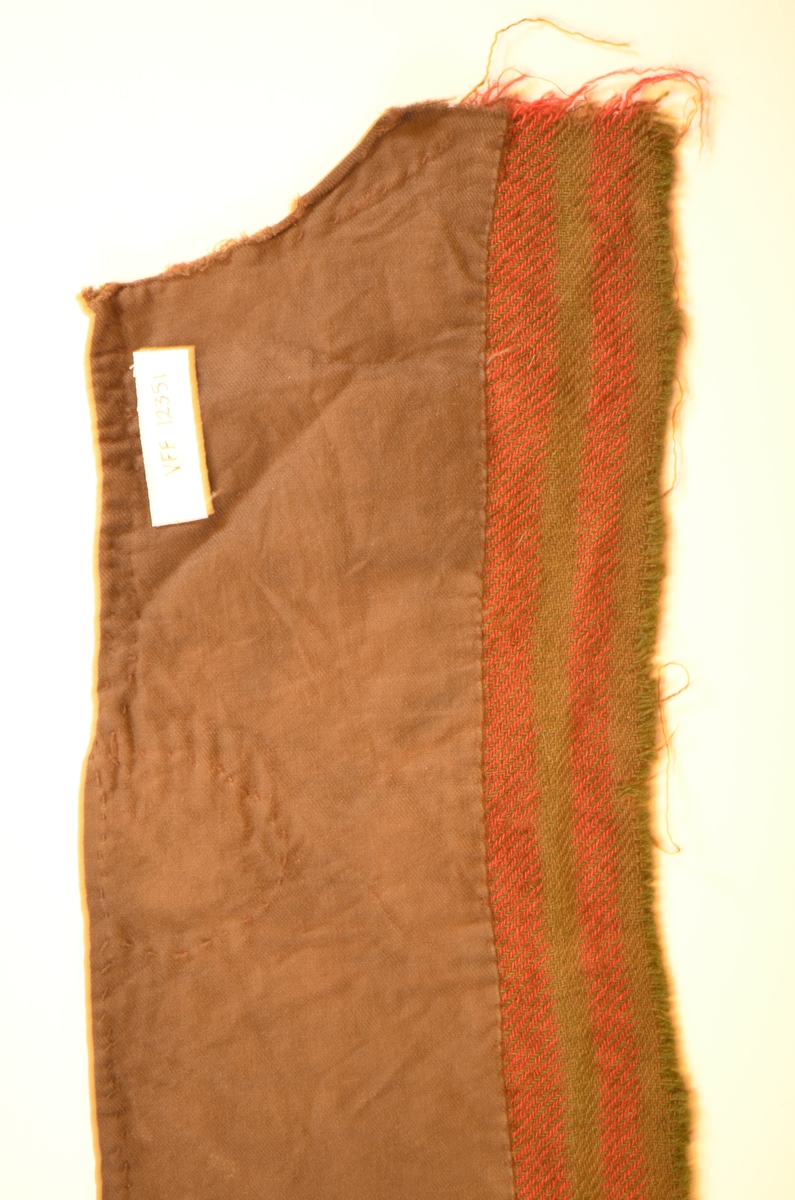 Stoffbit av ulltøy i brune, lilla og og grønne striper. Kypert-binding.
Fóra med brunt kypertvove bomullstøy.