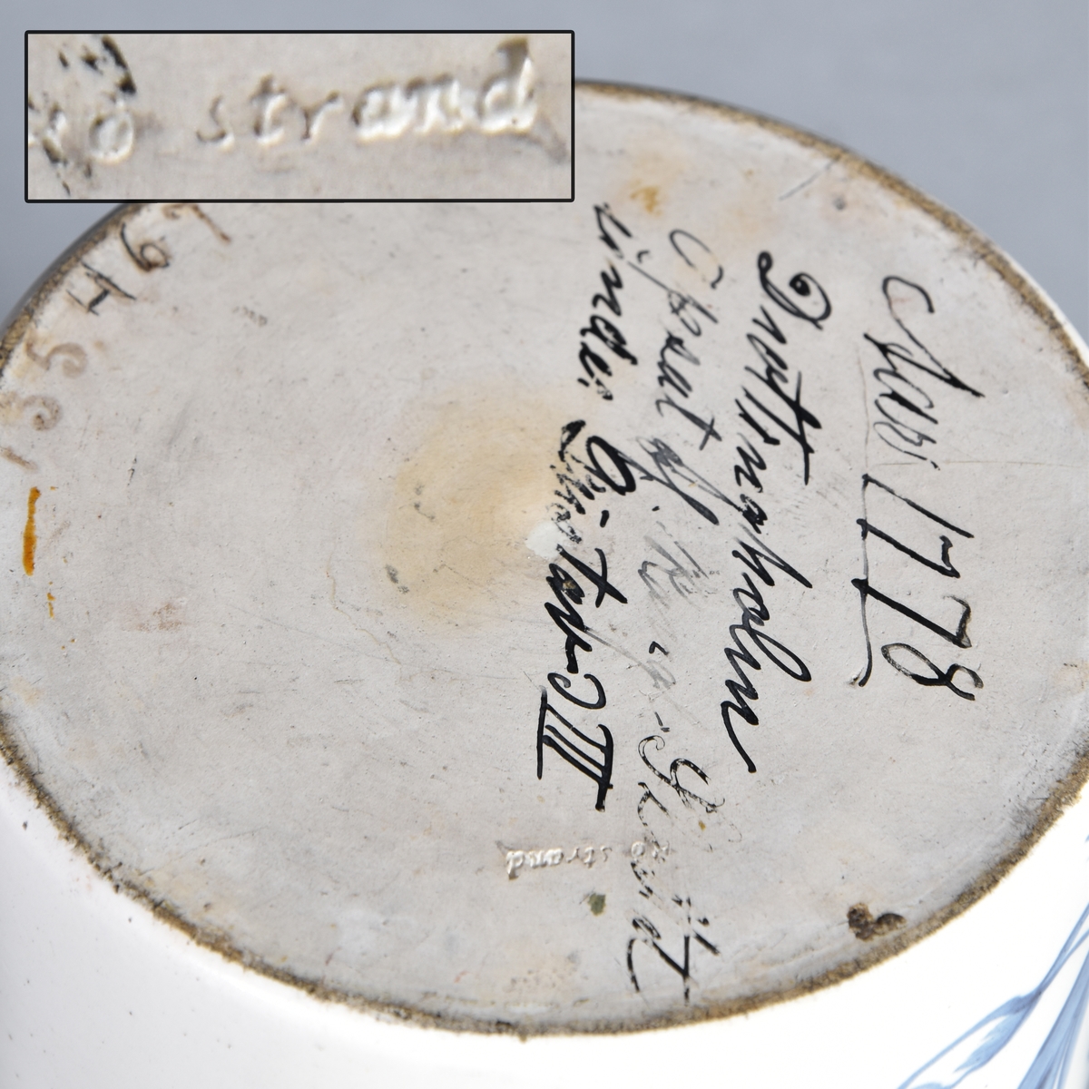Apoteksburk av vitglaserat flintgods, cylindrisk. Lock av papp, målat. Blå text inskriven i lagerbladskrans med krona.
