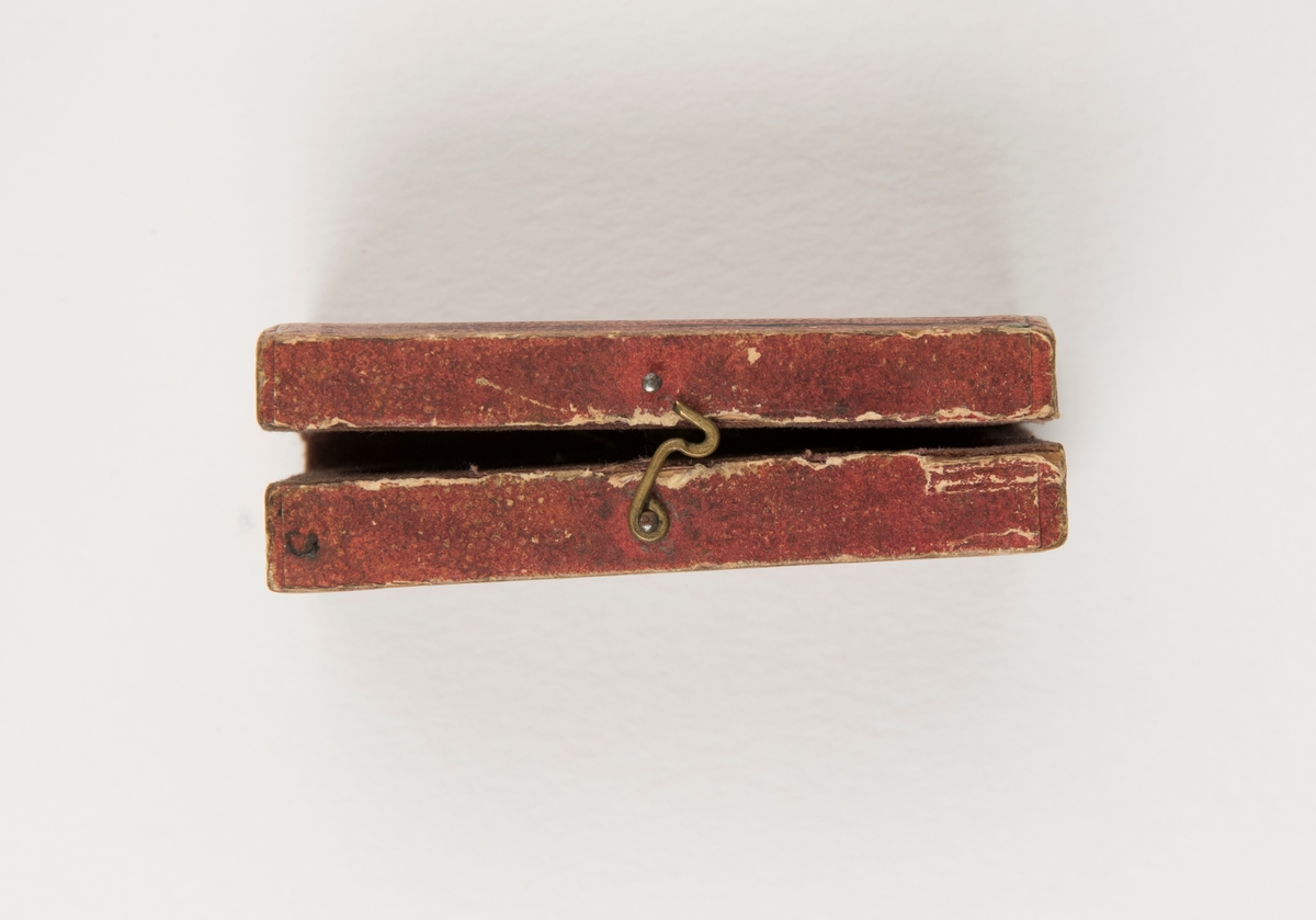 Snäppare av mässing och järn med mekanism för åderlåtning, förvaras i etui av trä. Etuiets utsida är klädd med rostbrunt papper och insidan är klädd med lila-rött sammet. Etuiet låses med en liten hasp.