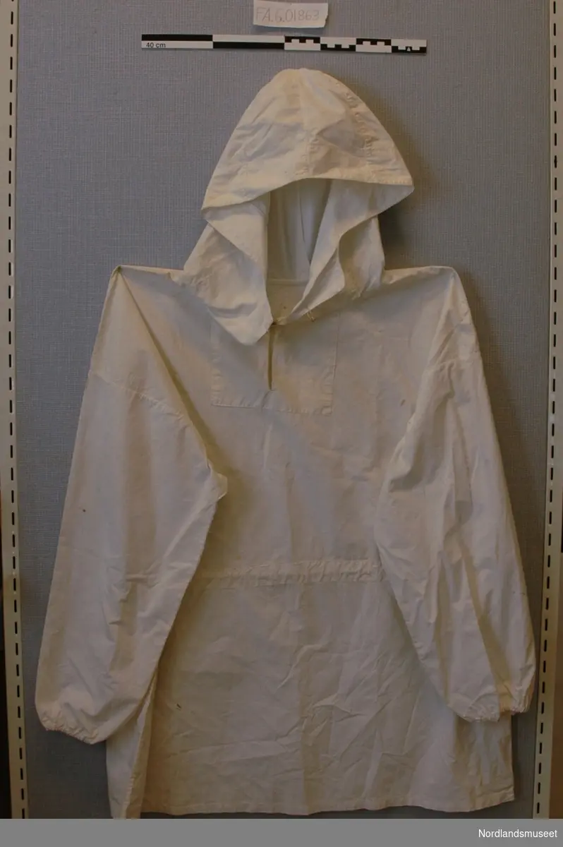 Hvit anorakk sydd av fallskjermstoff under 2. verdenskrig. Anorakken har hette og mulighet stramming i livet. Lukkes med en hempe i halsen.