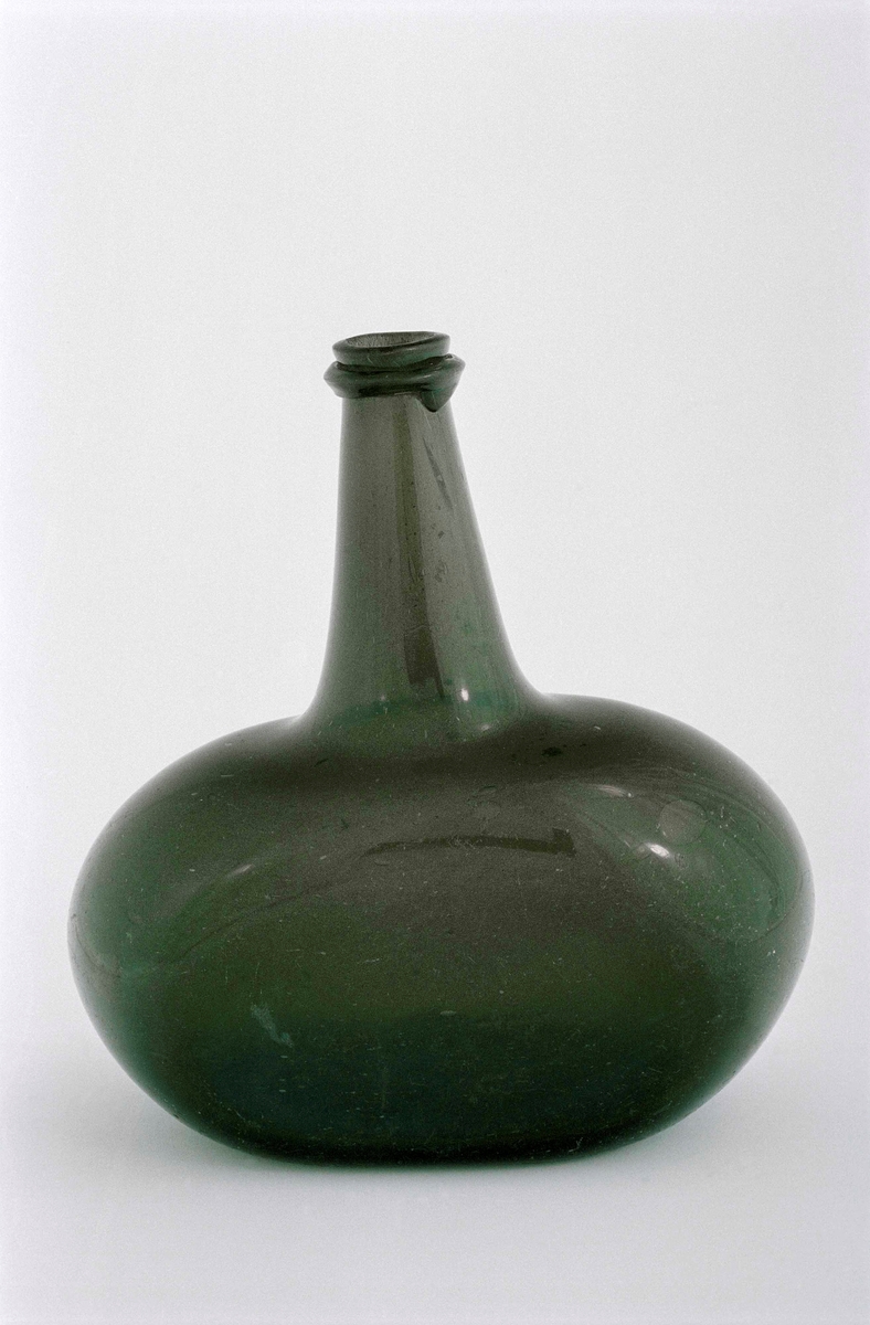 Flaska av grönt glas, oval med två platta sidor, lång hals med droppskydd, syffel i botten.