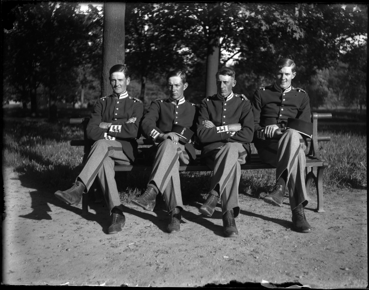 Fyra uniformklädda män sitter på en parkbänk med benen i kors. Bilden tagen under fotografen Harald Olssons excercistid.
