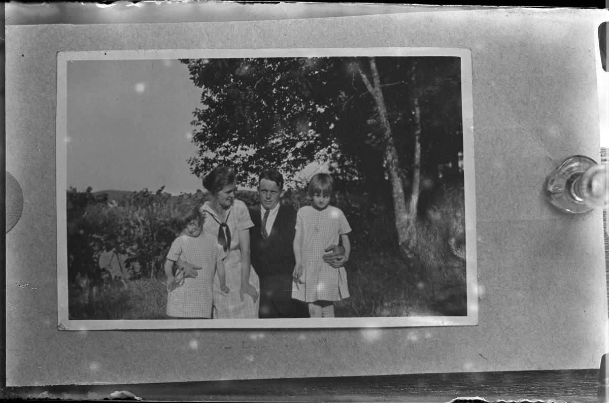 Reprofoto av bild på en kvinna, en man och två barn fotograferade utomhus. Kvinnan och barnen bär rutiga sommarklänningar medan mannen har kostym. I fotografens egna anteckningar står det "Rep. för Strandberg". Tolkat som Nils och Svea Strandberg med barnen Vivi och Kerstin.
