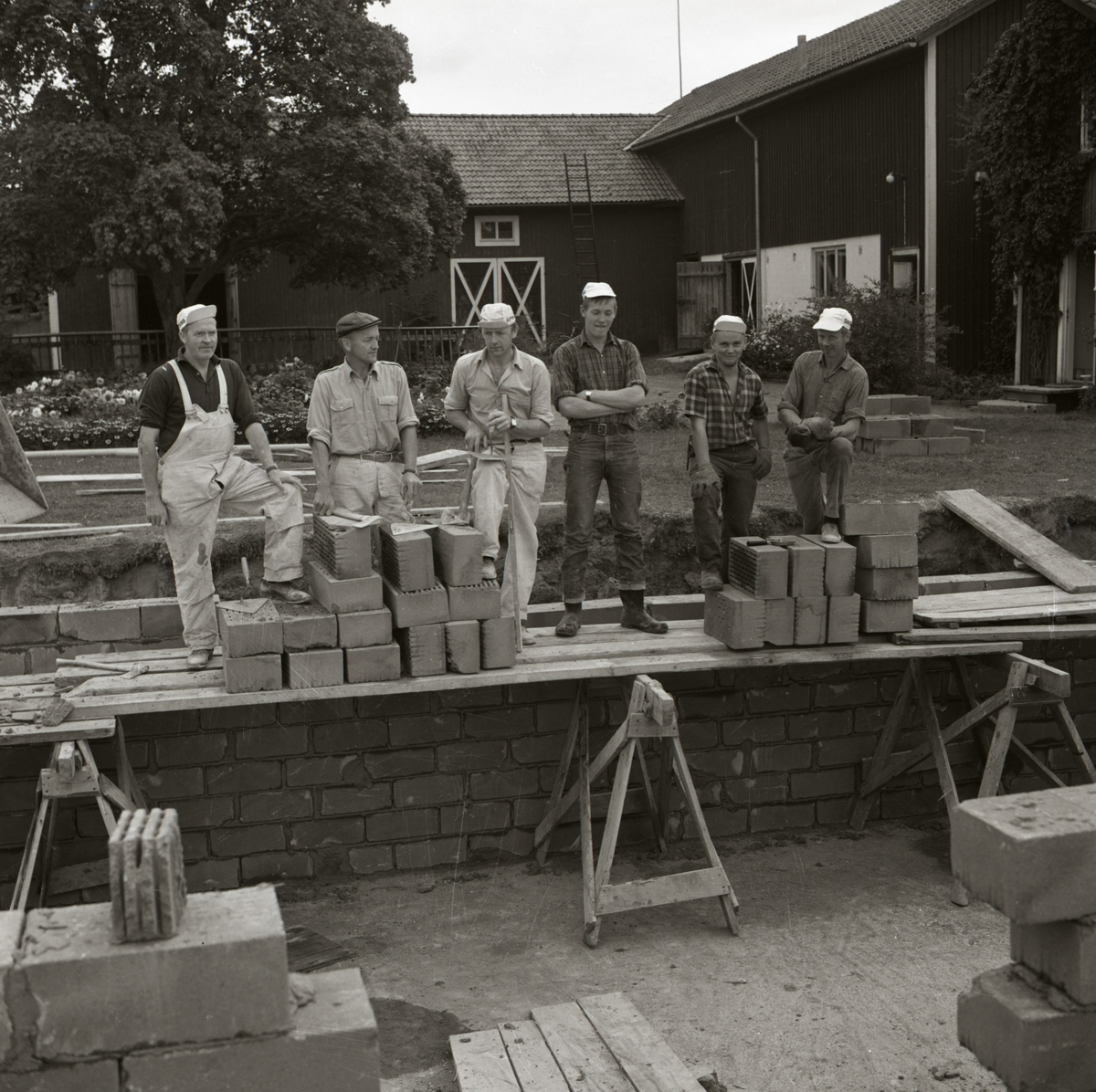 En grupp män pausar från sitt arbete med att mura tegel vid byggnationen av bostadshus vid gården Sunnanåker, 1967.