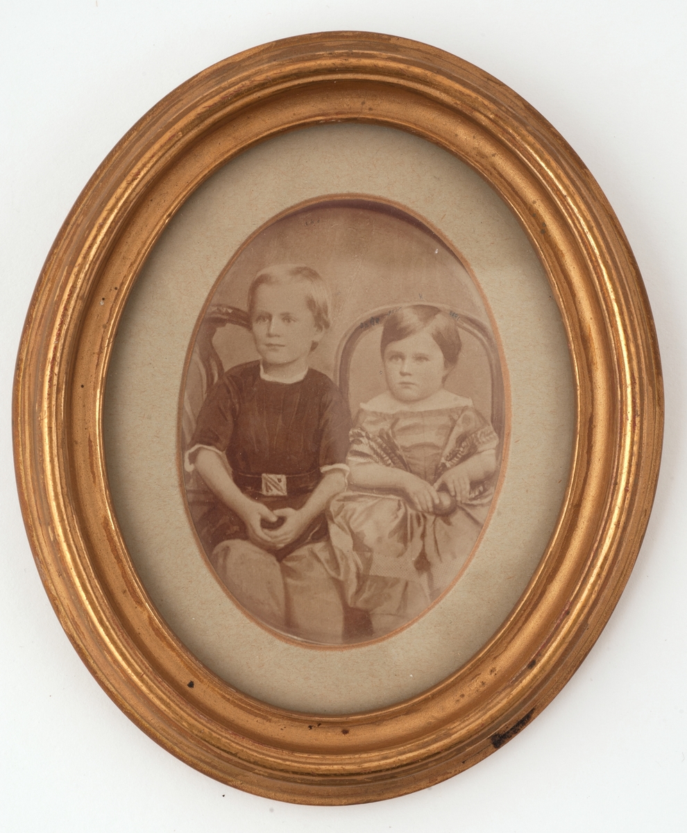 Portrett av gutt og jente sittende på stol.