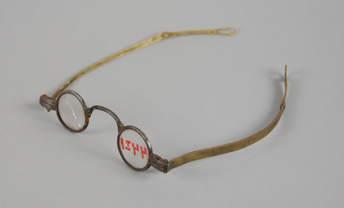 Briller med små ovale brilleglass og metallinnfatning. Brillestengene kan brettes ut.