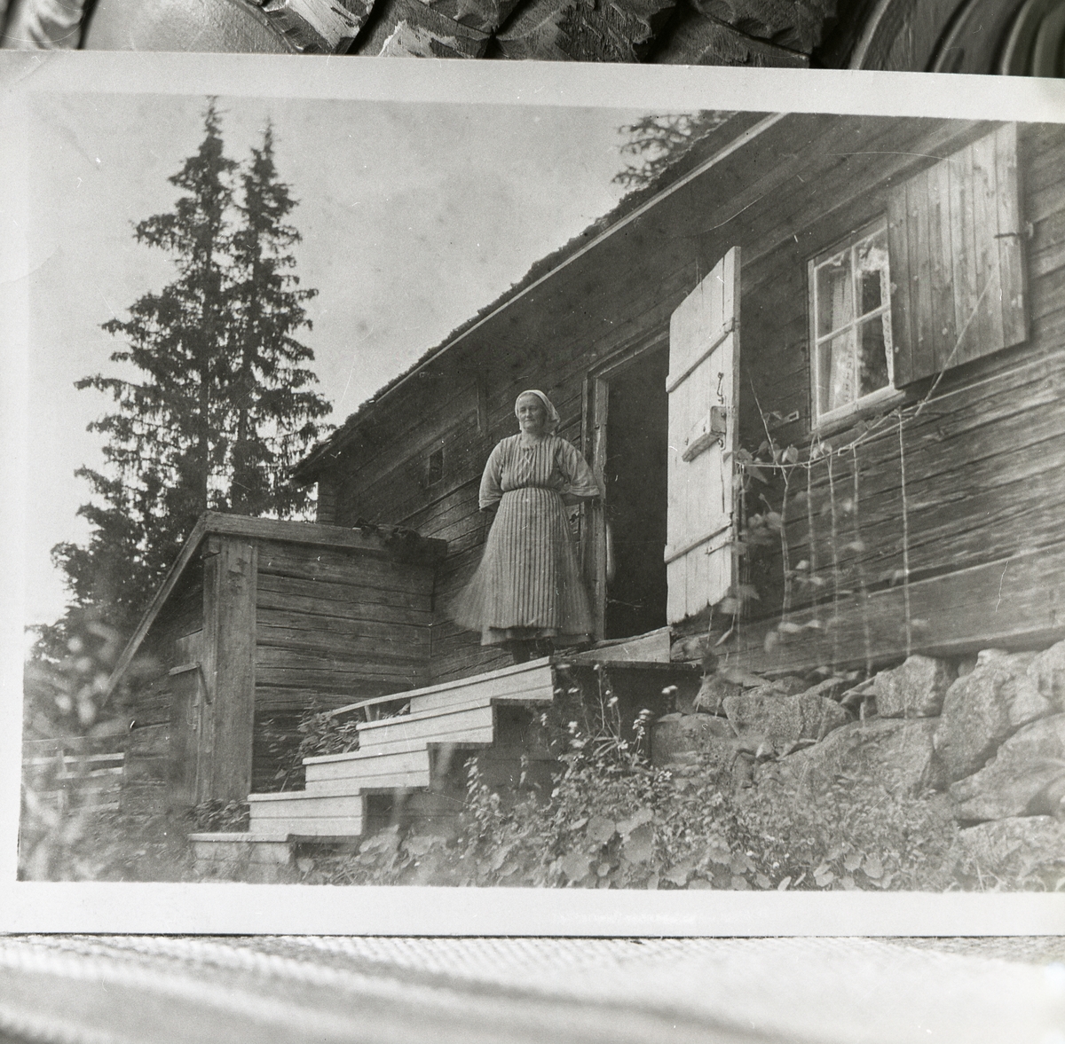 En kvinna står på trappan till en timmerstuga på fäbod i Flästa-Öjungen eller eventuellt Österbyvallen.