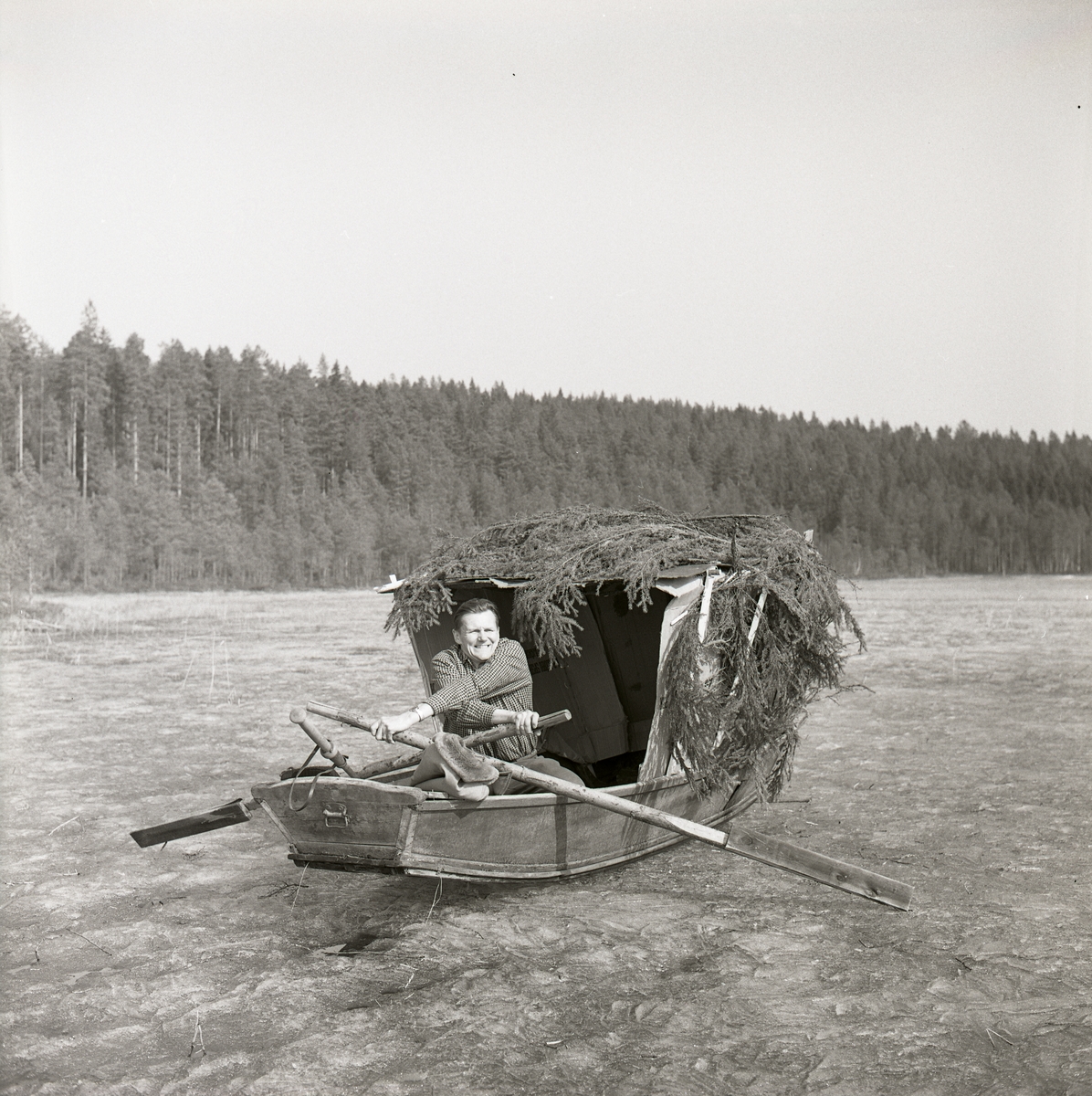 Hilding sitter i en eka med ett påbyggt glömsle och ror på en isbelagd sjö, Stråsjön april 1964.