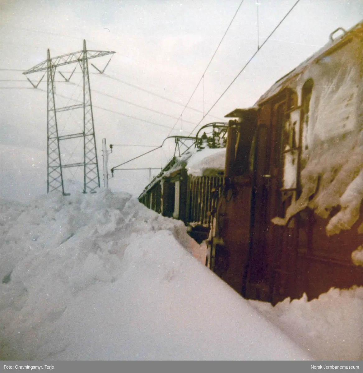 Nattoget fra Bergen til Oslo, tog 606, fastkjørt i snøen ved Oksebotn km 295, mellom Finse og Haugastøl. Toget ble trukket av diesellokomotiv type Di 3 nr. 607 og elektrisk lokomotiv type El 14 nr. 2188.