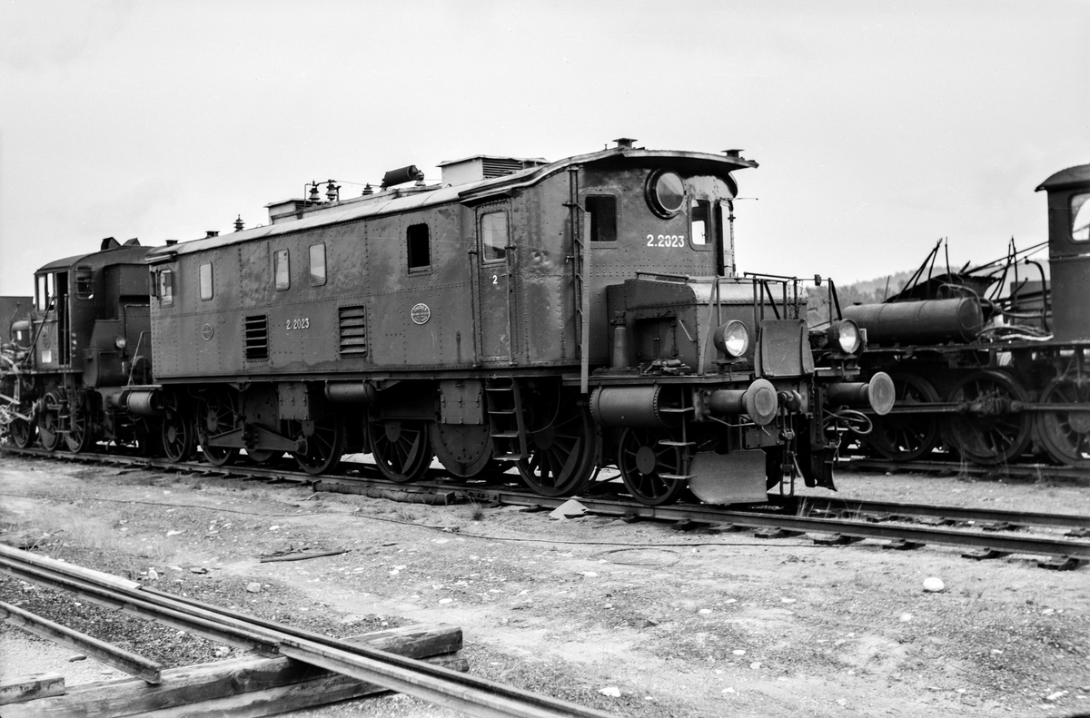 Utrangert elektrisk lokomotiv type El 2 nr. 2023 på huggeplassen på Grorud Verksted. Bak sees hensatt og delvis demontert damplokomotiv type 40a nr. 462 ("Kamelen").