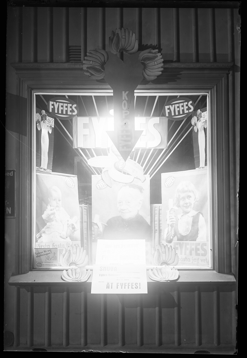 Ett upplyst skyltfönster med reklam för Fyffes bananer. I fotografens anteckningar står det "Köhlers affär".