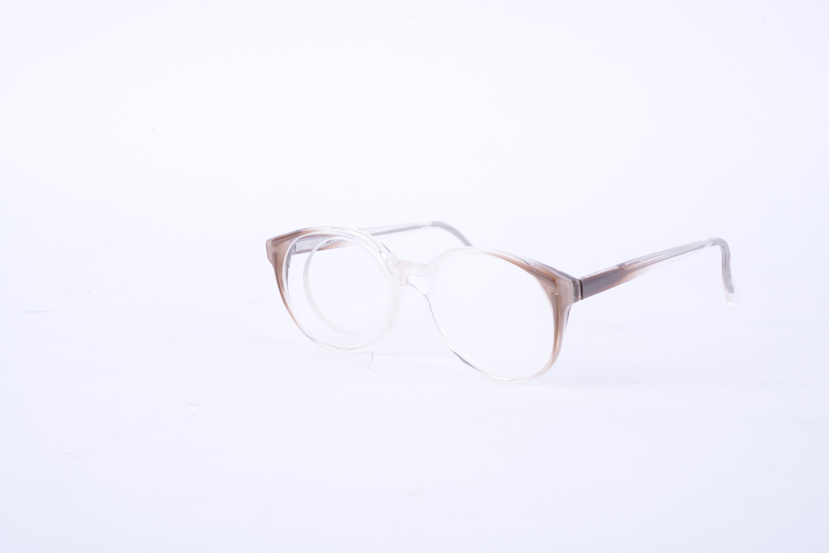 Brille i hvit og brun plast med frostet glass på venstre side. Glass med hull for å sette inn ulike linser på høyre side.