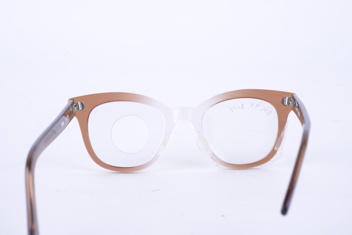 Brille i hvit og brun plast med frostet glass på høyre side. Glass med hull for å sette inn ulike linser på venstre side.