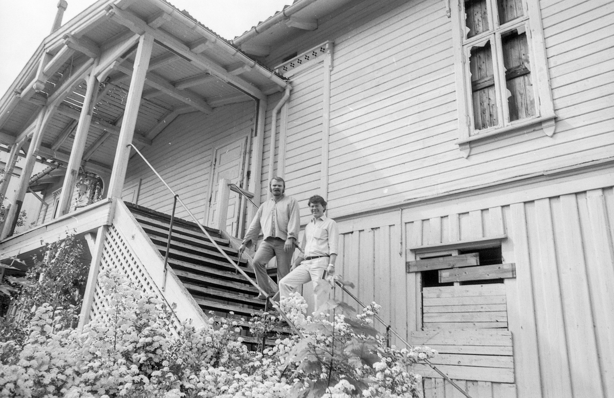Festiviteten i Drøbak. Verneverdig toetasjes trebygning med tretrapp og jernrekkverk. Blomstrende busk ved trappen. Per Svendsen sitter på trappetrinnet. Jan Wold Hansen og Stein Skjelle på trappen.
