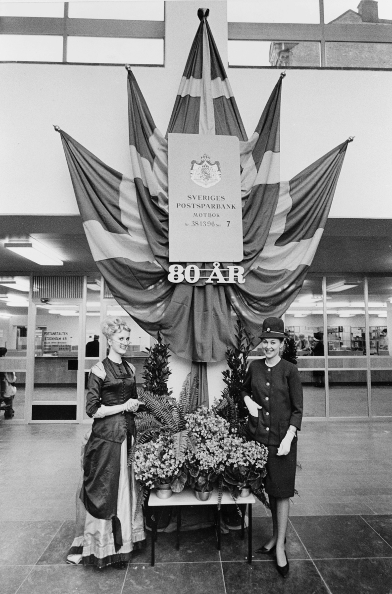 Postbanken firar sitt 80-årsjubileum i år. Fru Solveig Östergren, klädd som kontorsdam från anno dazumal, och hennes kollega av idag fröken Monica Johansson, i entréhallen på nedre botten.