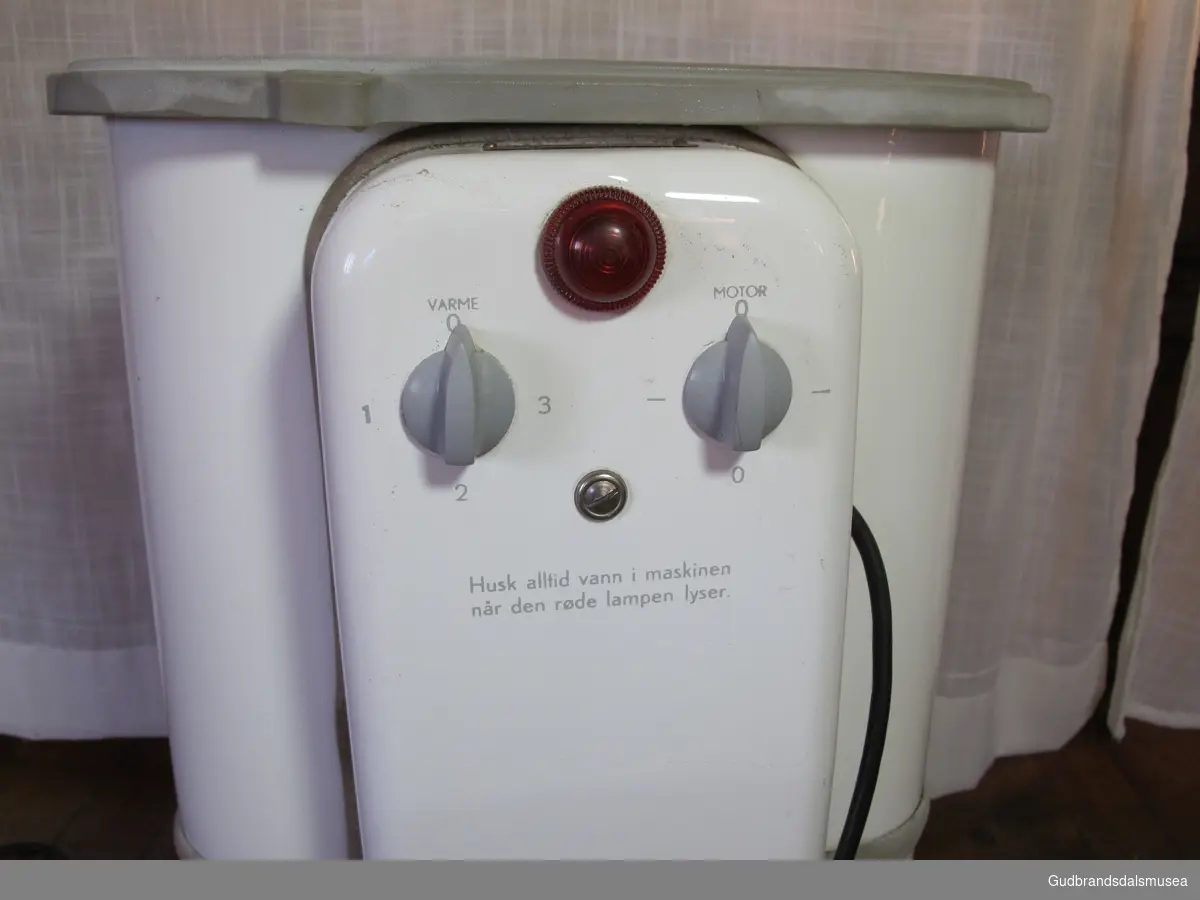 Elektrisk vaskemaskin med lokk på toppen. Merket Evalet. På baksiden er det to brytere. En for varme og en for motor. Nede i maskinen er det en rotor - formet som et tett hjul. Slangen for tapping av vann er brekt av.  Maskinen er emaljert. Har  et rødt "øye" på baksiden. En vaskestav følger med.