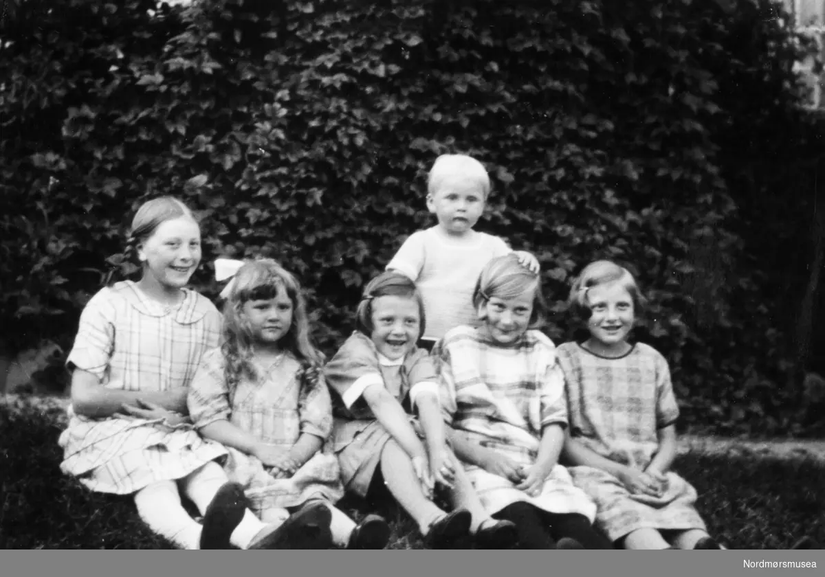 Foto av en gruppe barn sittendeute i hagen. Fra Fru Williams fotoalbum. Eier av originalmaterialet er Gunnar Williams. Fra Nordmøre museums fotosamlinger.