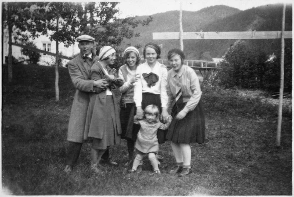 Gruppebilde av fire kvinner, et barn og mann med pipe som står i en hage. Rundt 1930.