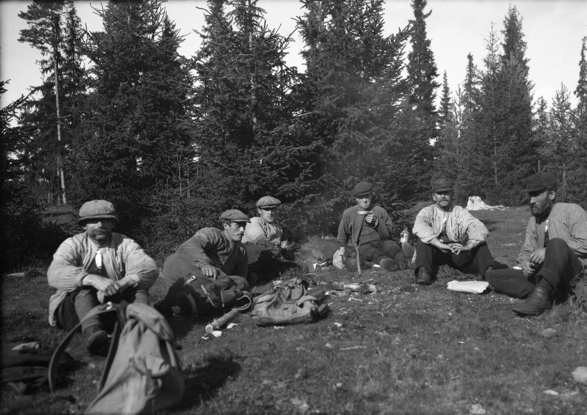 Seks menn slapper av i skogen (skogsarbeidere).