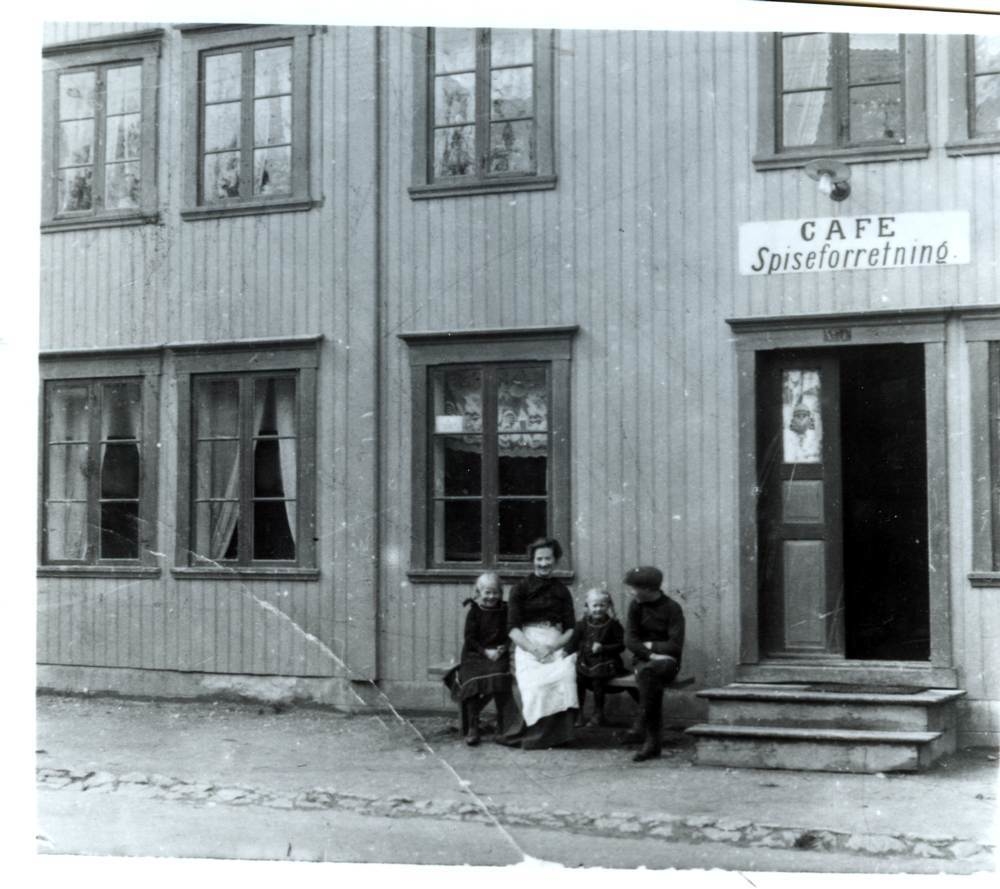 Personer på benk utenfor Olga Andersens spiseforretning (Tippen) i Strandgata.