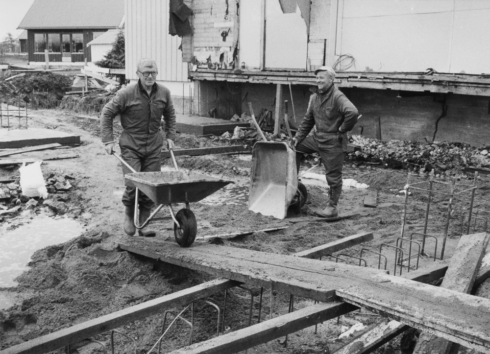 Byggevirksomhet i Leirfjord. To mann med trillebårer på byggeplass.