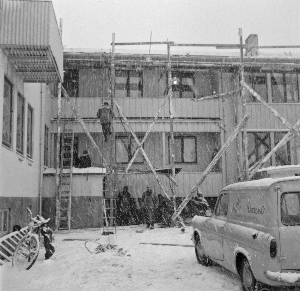 Entreprenør Drevland utfører byggearbeid/renovering ved Vefsn Sykehus. Stilas oppsatt langs veggen og arbeidsfolk. Snøvær.