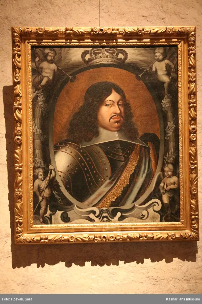 Porträtt, bröstbild av Karl X Gustav i rustning. Vit, stärkt krage, över vänstra axeln ett draperi eller värjgehäng. Oval målad inramning med putti och lagerkransar. Över ovalen en krona, nedan början till textkartusch.