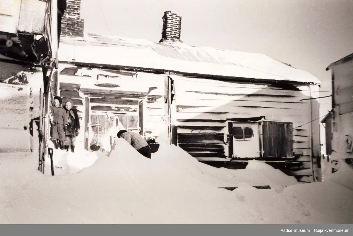 Åse Martinsen med venninne står i hjørnet på Tuomainengården mens ant. Karl Tuomainen måker snøen foran. Ca 1952-1954.