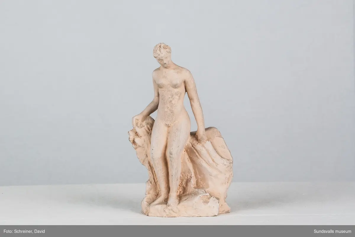 En skulptur i form av en naken kvinna som lutar sig emot ett staket.