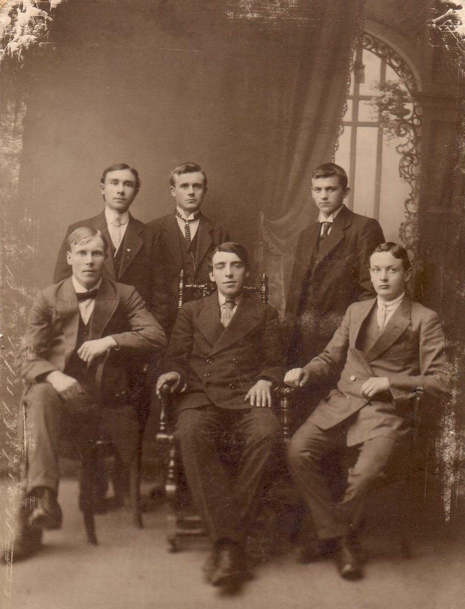Gruppeportrett av seks menn. Sittende ytterst til høyre Egill Christensen og sittende til venstre Alf Aarnes. I midten en fetter som utvandret til USA. Ca 1915 i Kirkenes.