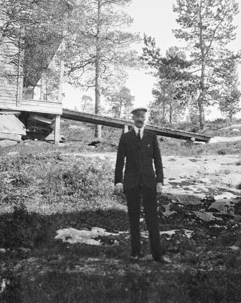 Kong Haakon VII ved Svenningheimen.   Kongen var iført mørk dress, kvit skjorte og slips, samt lue med blank skygge.  Han poserte for fotografen på en skyggeflekk på ellers solbestrålt lyngmark med enkelte snøflekker.  I bakgrunnen ser vi en forholdsvis høy bygning med lasterampe langs langveggen med oppkjøringsbru av tre.  På bakkekammen bakenfor vokste det enkelte furutrær. 

Svenningheimen ble bygd i 1888 for The north of Europe Land and Mining co. limited, som eide store utmarksarealer på denne delen av Helgeland. Stedet, som lå mellom Øvre og Nedre Svenningvatn, ble under navnet «Svenninghouse» brukt som innkvarteringssted de engelske eierne, deres venner og forretningsforbindelser samt andre fisketurister.  Denne bruken fortsatte også etter at det norskeide Nesbruket overtok utmarkseiendommene i Grane og Vefsen omkring 1900.  Nesbruket med gjenværende eiendomsportefølje ble solgt til staten i 1920.