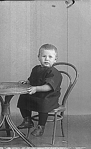 Tage Jansson, en liten pojk som sitter på en rottingstol vid ett bord av samma material.