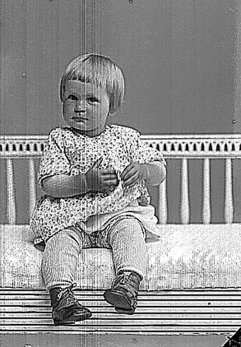 Märta Jansson, en liten flicka i klänning sittande på en soffa av sengustavianskt snitt.